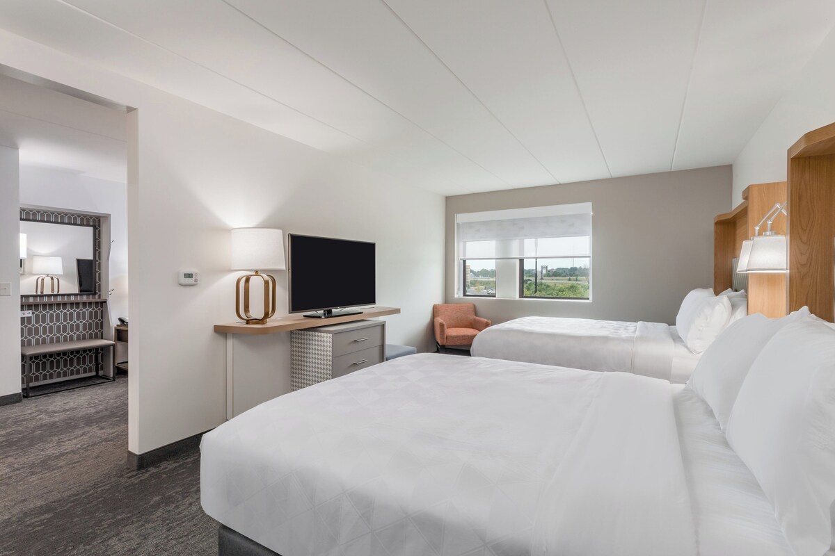 Habitación de hotel con dos camas, televisión, escritorio con lámpara y ventana con vistas.