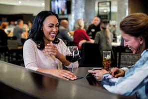 A bar setting with a person gesturing and another holding a glass of red wine.