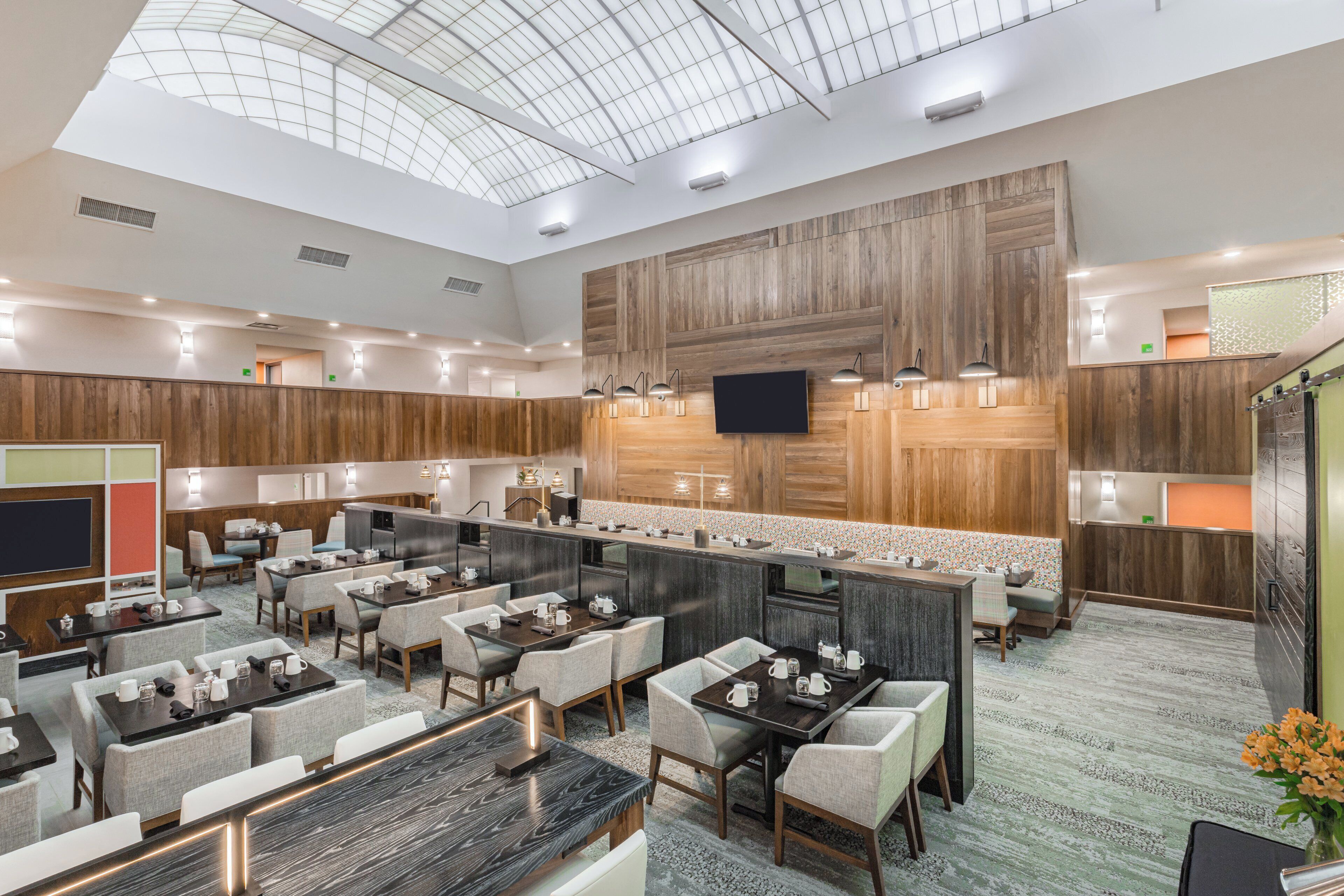 A modern hotel lobby with a high ceiling, a central bar area, and multiple seating arrangements.
