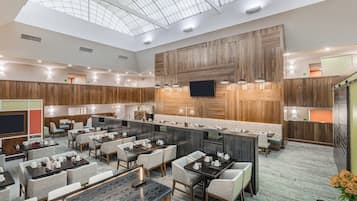 A modern hotel lobby with a high ceiling, a central bar area, and multiple seating arrangements.