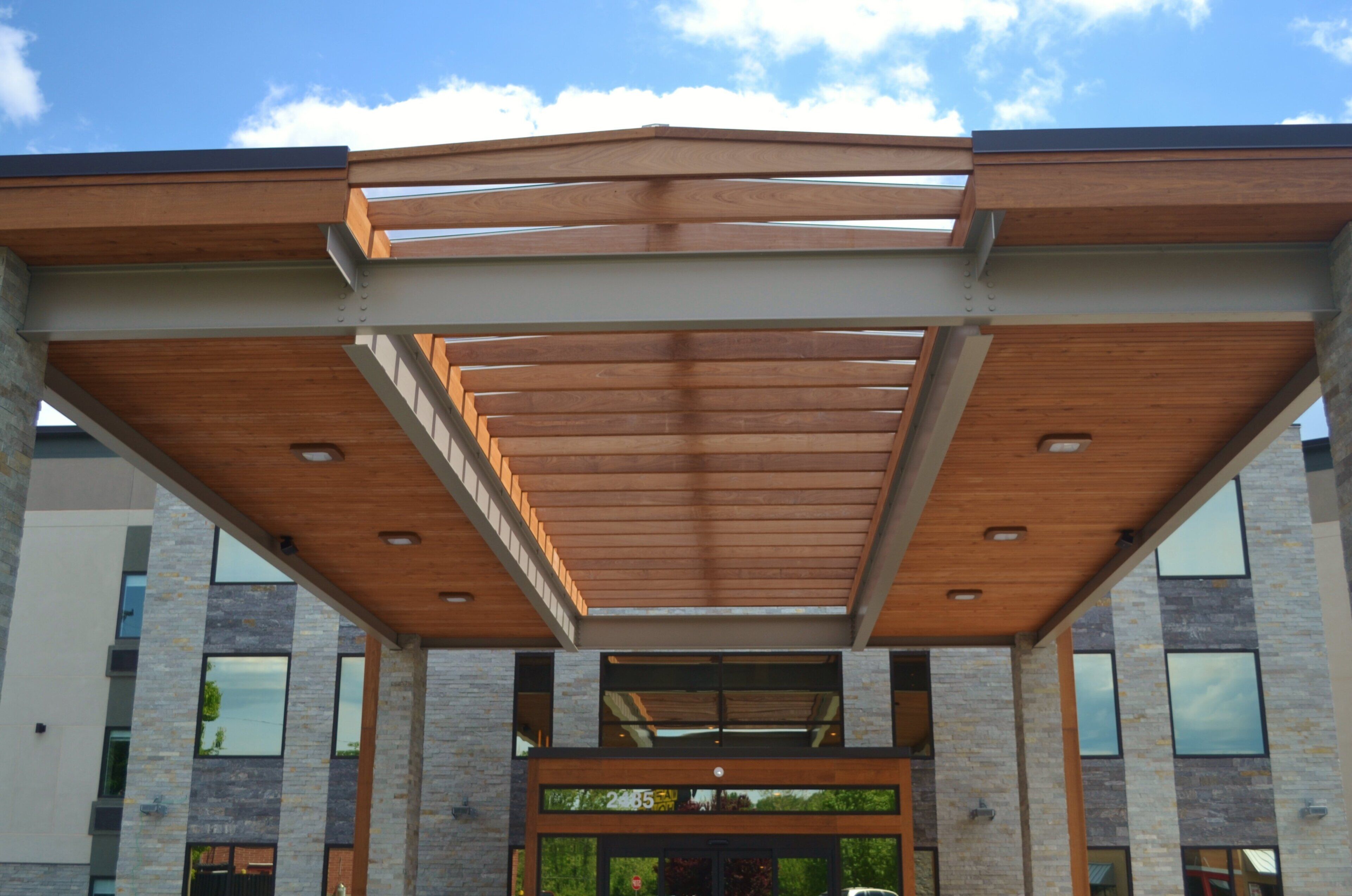 Un edificio moderno con estructura de pérgola de madera, ventanas grandes y fachada de piedra.
