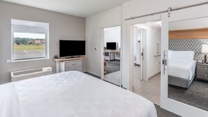 Une chambre d’hôtel moderne, dotée d’un grand lit, d’un bureau avec un ordinateur, d’une télévision et offrant une vue sur le parking par une fenêtre.
