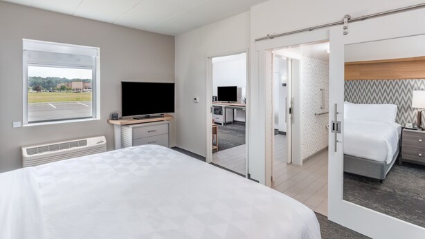 A modern hotel room with a large bed, a desk with a computer, a TV, and a view of the parking lot through a window. - Holiday Inn Columbus by IHG (Columbus)