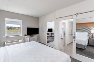 Una habitación de hotel moderna con una cama grande, un escritorio con computadora, un televisor y vista al estacionamiento a través de una ventana.