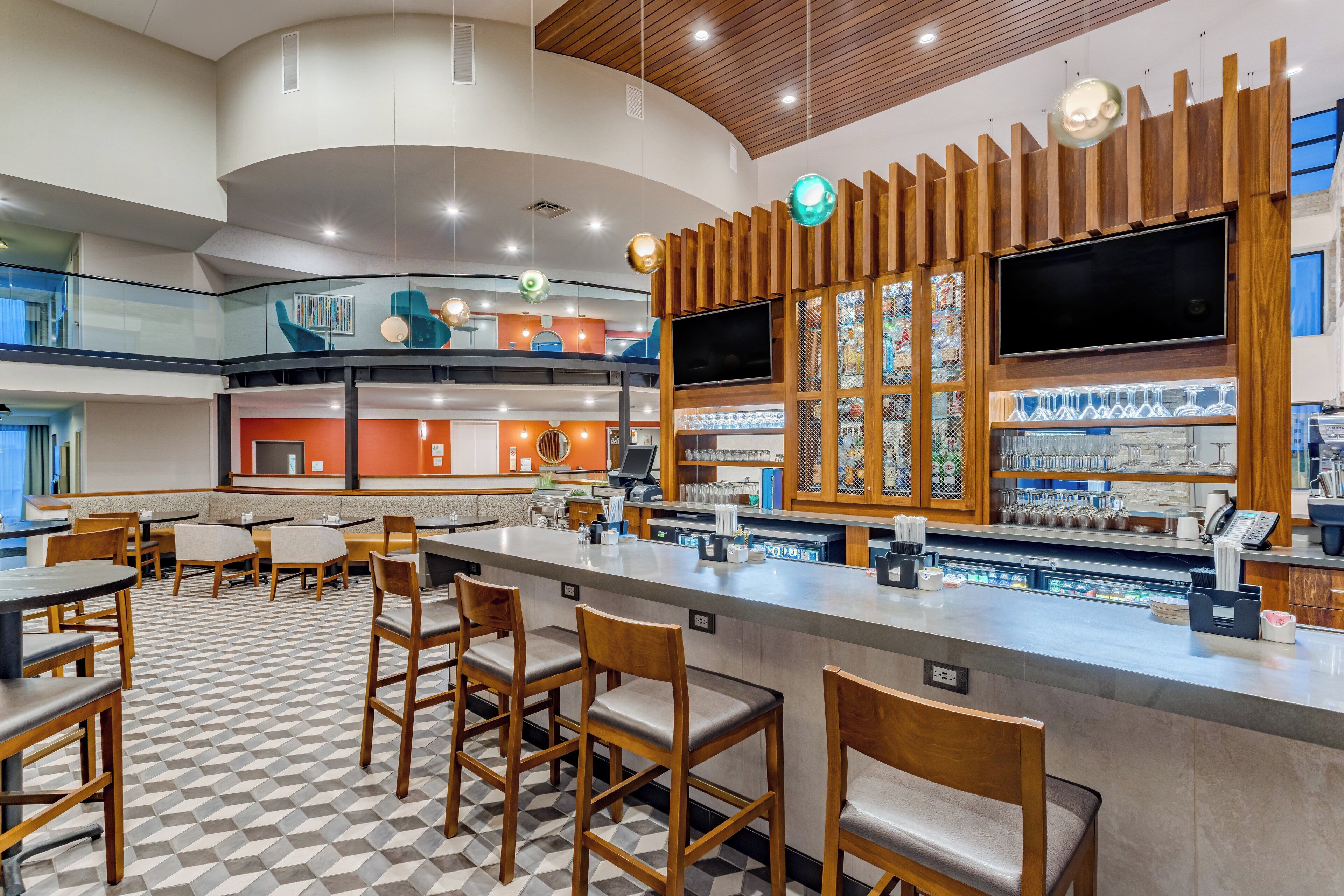 Zona de bar moderna con piso a cuadros, taburetes de madera y una barra con cristalería.