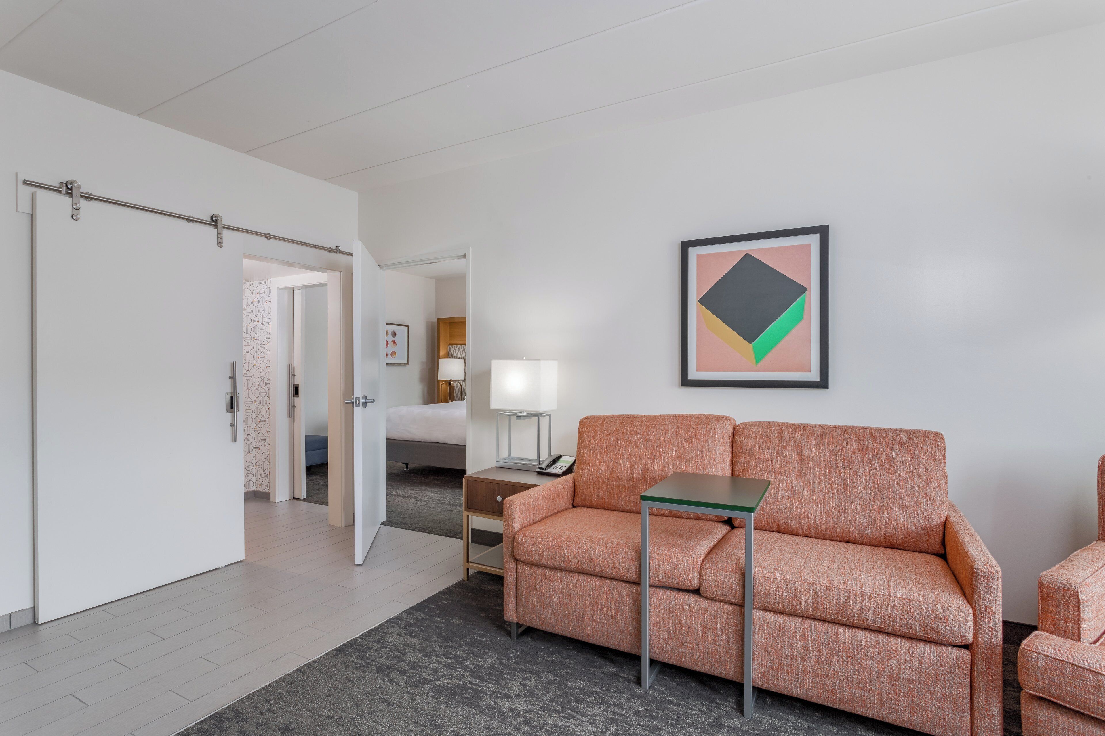 A hotel room with a sofa, a small table, a bed, and a bathroom visible through an open door.