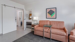 Une chambre d’hôtel moderne, équipée d’un canapé, d’une petite table, d’une lampe et d’une œuvre d’art abstraite encadrée au mur.