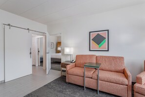 A modern hotel room with a sofa, a small table, a lamp, and a framed abstract artwork on the wall. - Holiday Inn Columbus by IHG (Columbus)