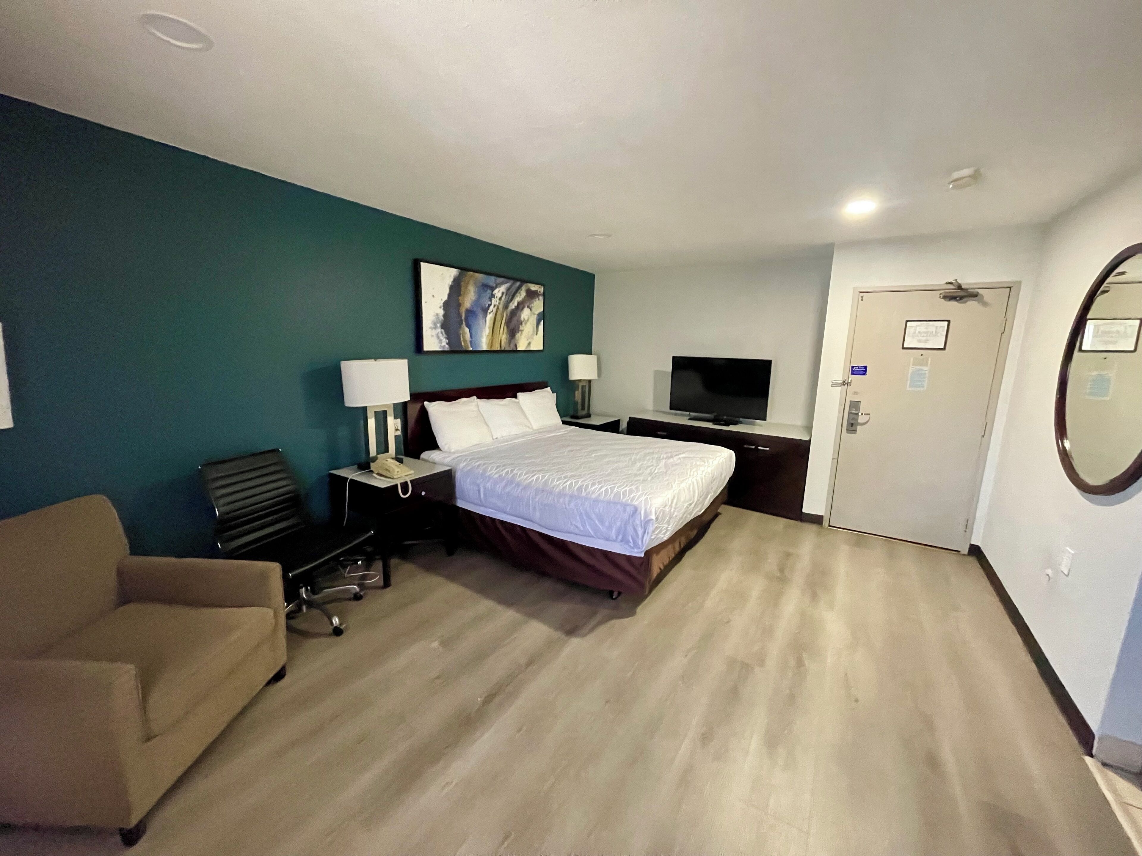 Une chambre d’hôtel avec un lit, deux tables de chevet, une télévision, un bureau, une chaise et une porte.