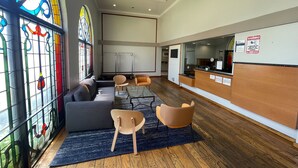 A modern waiting area with a reception desk, seating, and a large stained glass window. - Portside Inn & Suites (San Pedro)