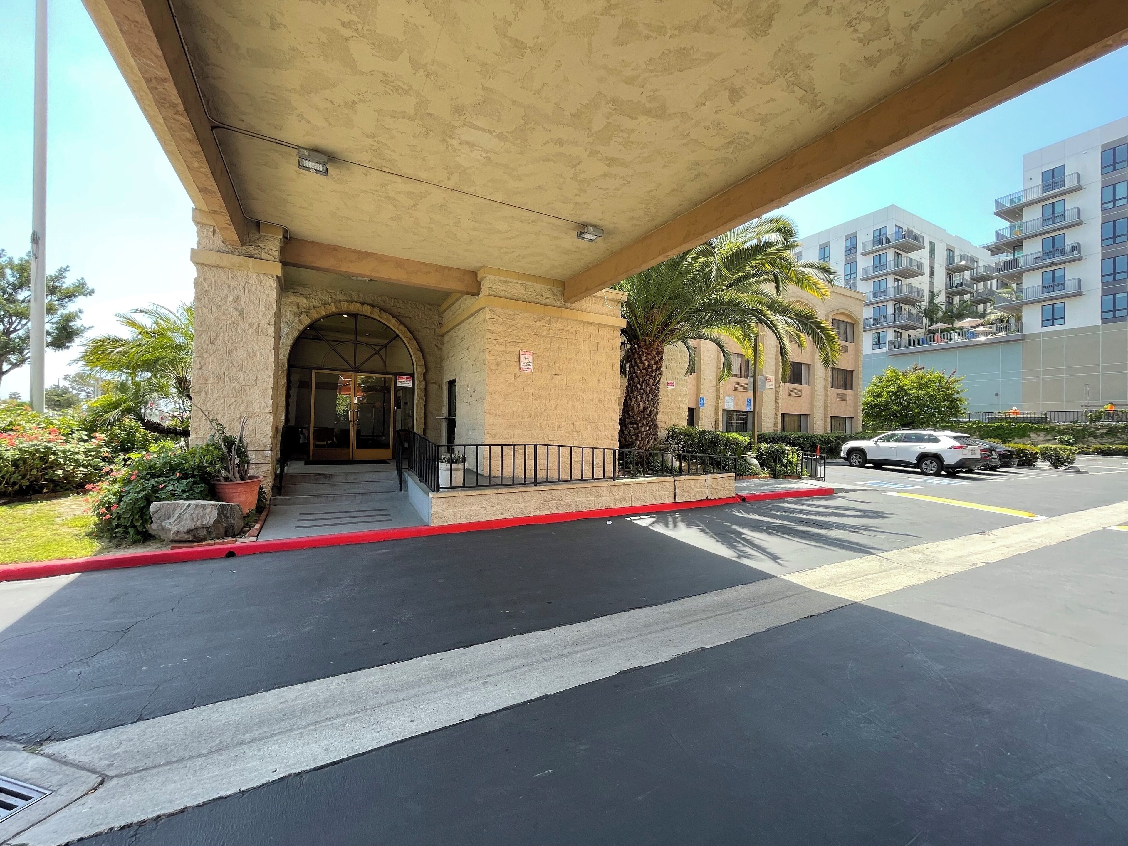 A hotel entrance with a stone facade, a covered walkway, and a parking area.
