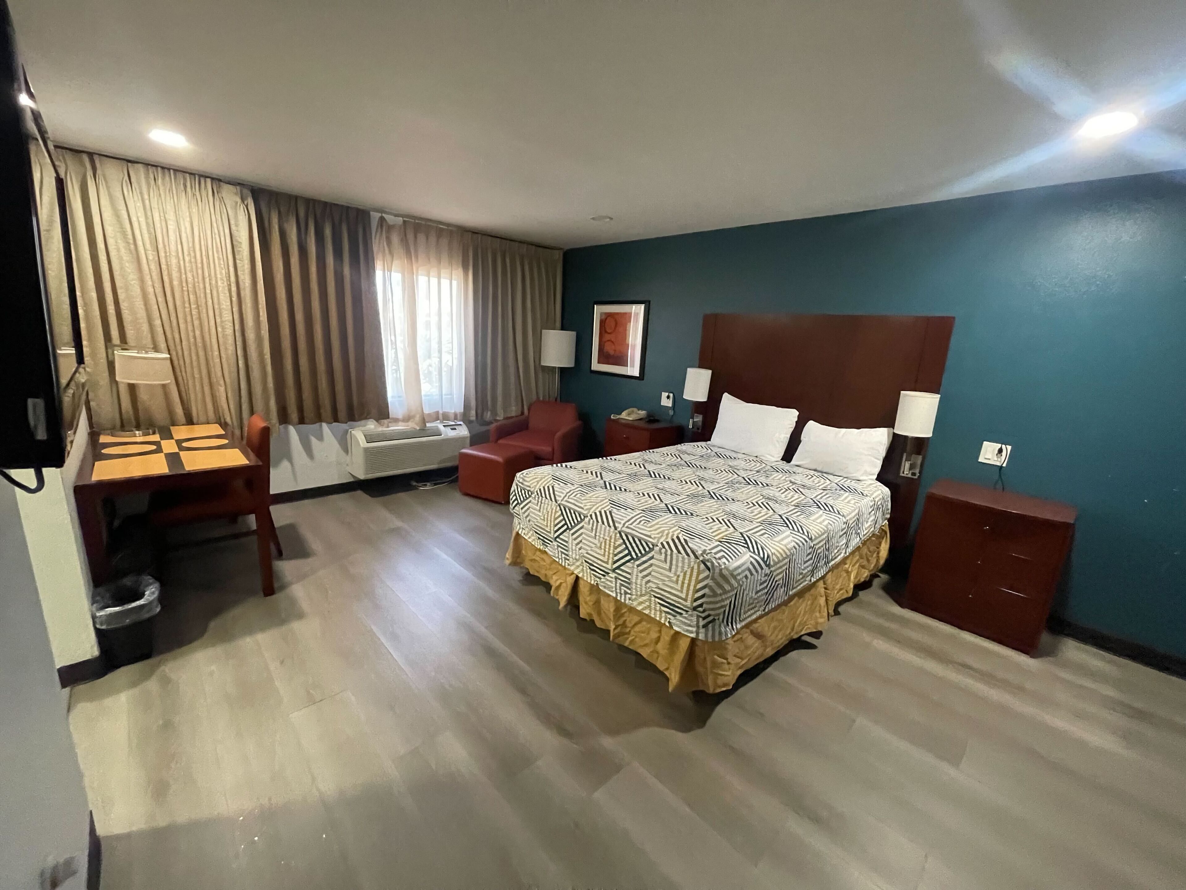 A hotel room with a bed, a desk, a chair, a lamp, and a window with curtains.