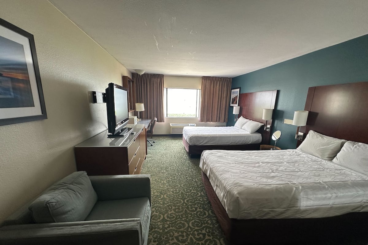 Ein Hotelzimmer mit zwei Betten, einem Schreibtisch, einem Fernseher und einem Sofa.