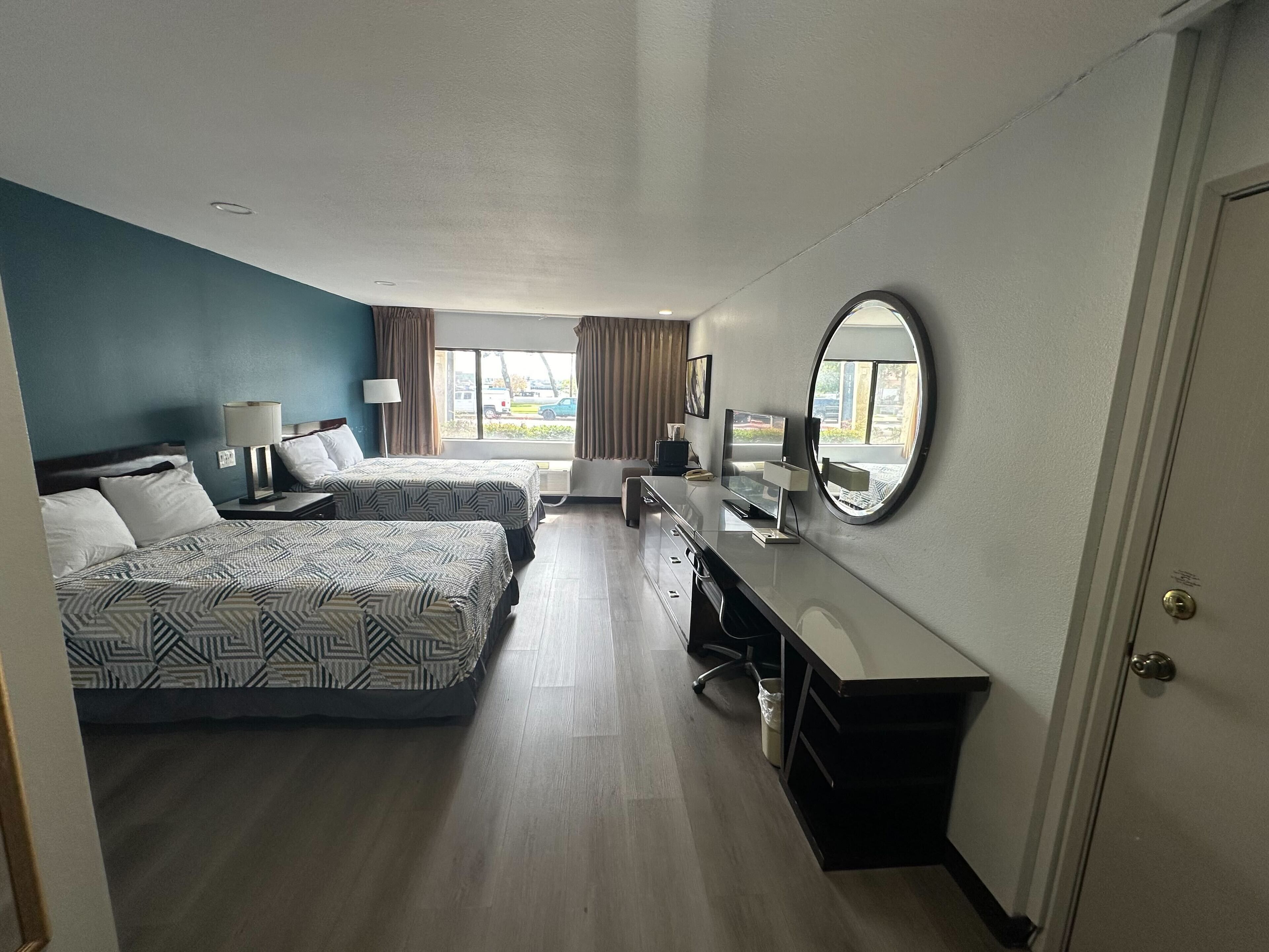 A hotel room with two beds, a desk, a mirror, and a view of the street.