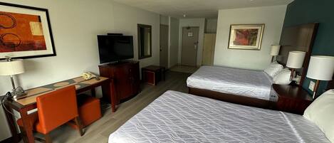Una habitación de hotel con dos camas, un escritorio con silla, un televisor y una lámpara de escritorio.