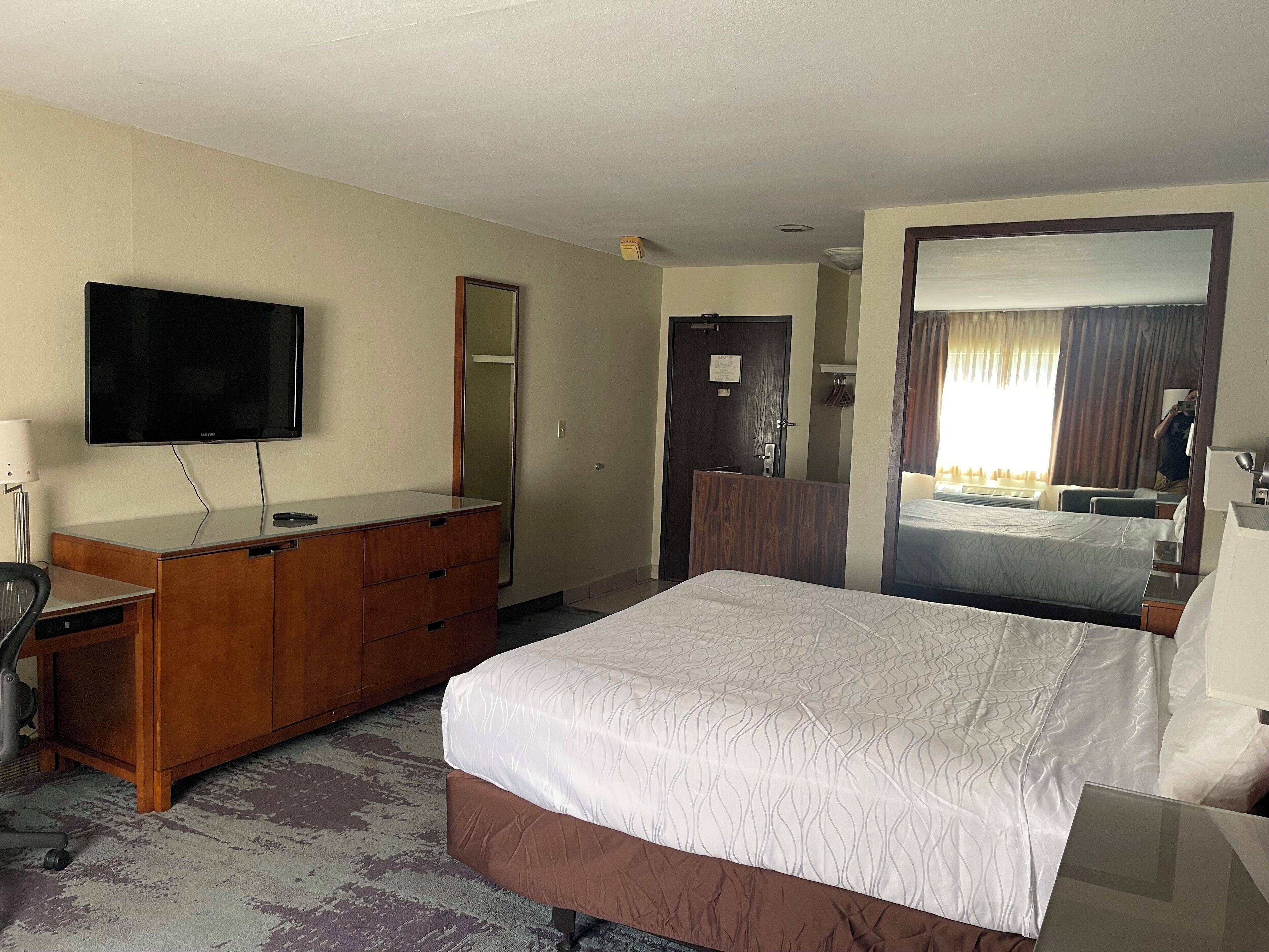 Habitación de hotel con cama, televisión, cómoda y espejo.
