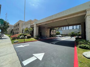 A hotel entrance with a covered walkway, a parking lot, and a clear sky. - Portside Inn & Suites (San Pedro)