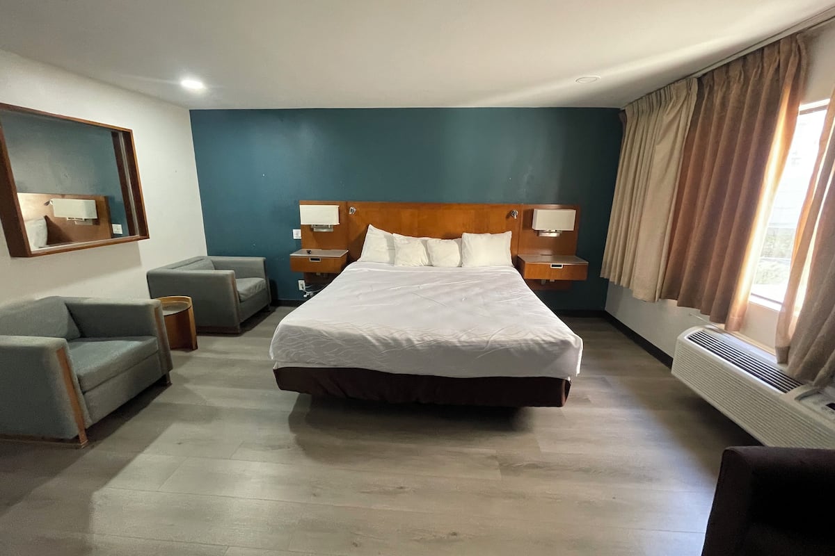Ein Hotelzimmer mit einem großen Bett, einer Couch, einem kleinen Tisch, einem Spiegel und einem Fenster mit Vorhängen.