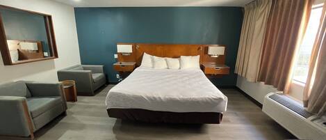 Habitación de hotel con una cama grande, un sofá, una mesita, un espejo y una ventana con cortinas.