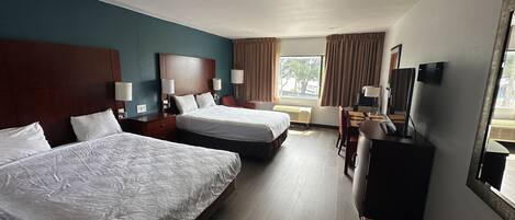 A hotel room with two beds, a desk, a chair, a TV, and a window with curtains.