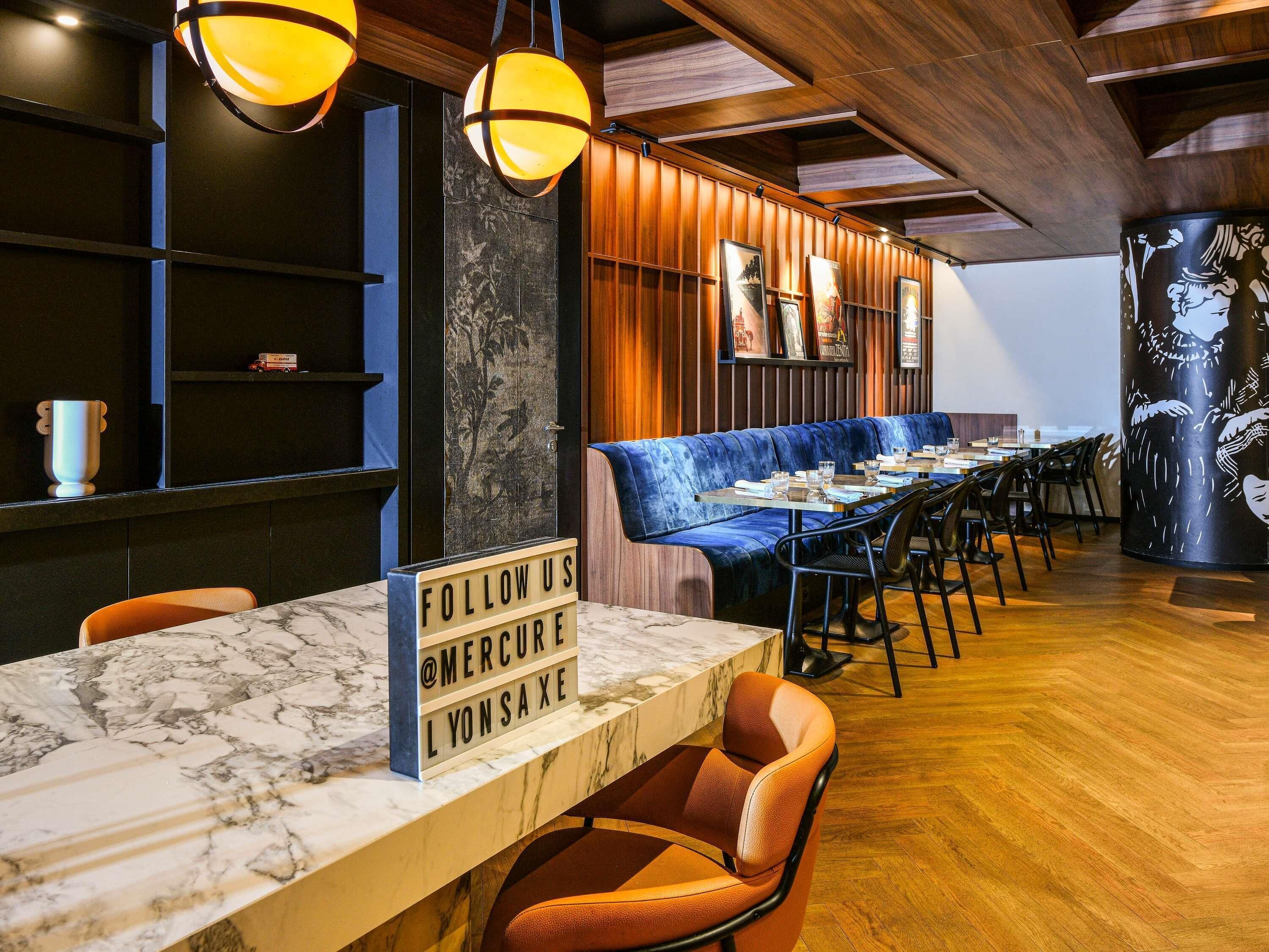 Ein Restaurant mit Marmorplatte, blau gepolsterten Sitzmöglichkeiten und hängenden Pendelleuchten.
