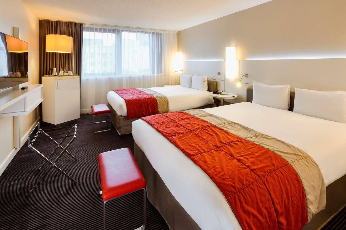 Camera d'albergo con due letti, una scrivania, una sedia, una televisione e una finestra con tende.