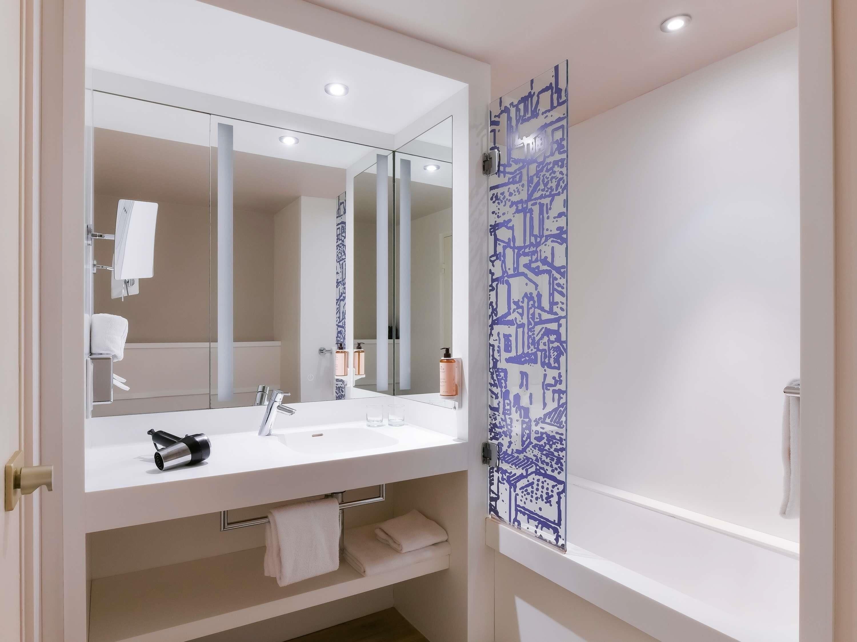Un baño moderno con un espejo grande, lavamanos blanco y un panel decorativo azul.