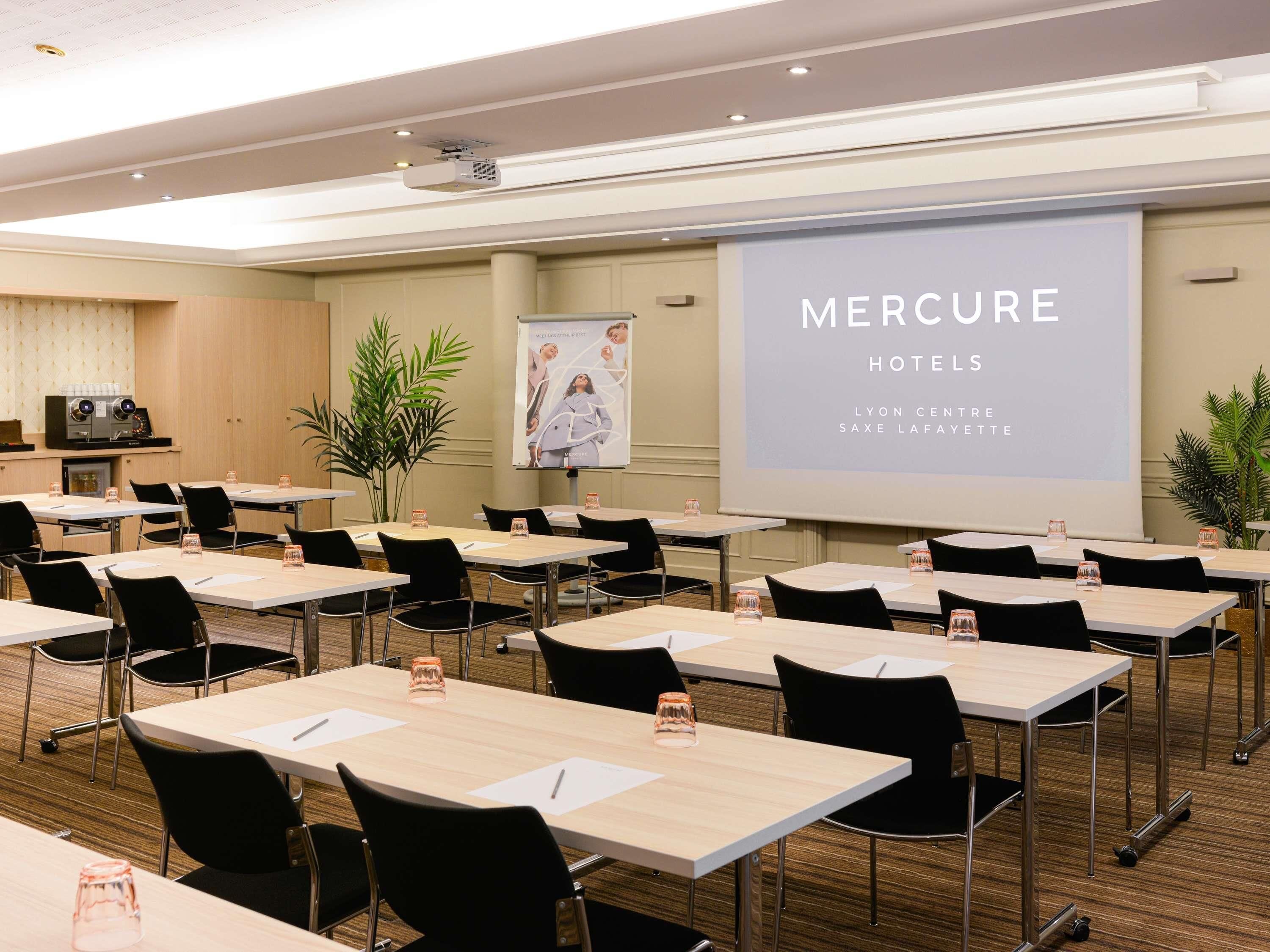 Une salle de conférence équipée de tables, de chaises, d’un écran de projection et d’une banderole aux couleurs de la chaîne hôtelière Mercure.