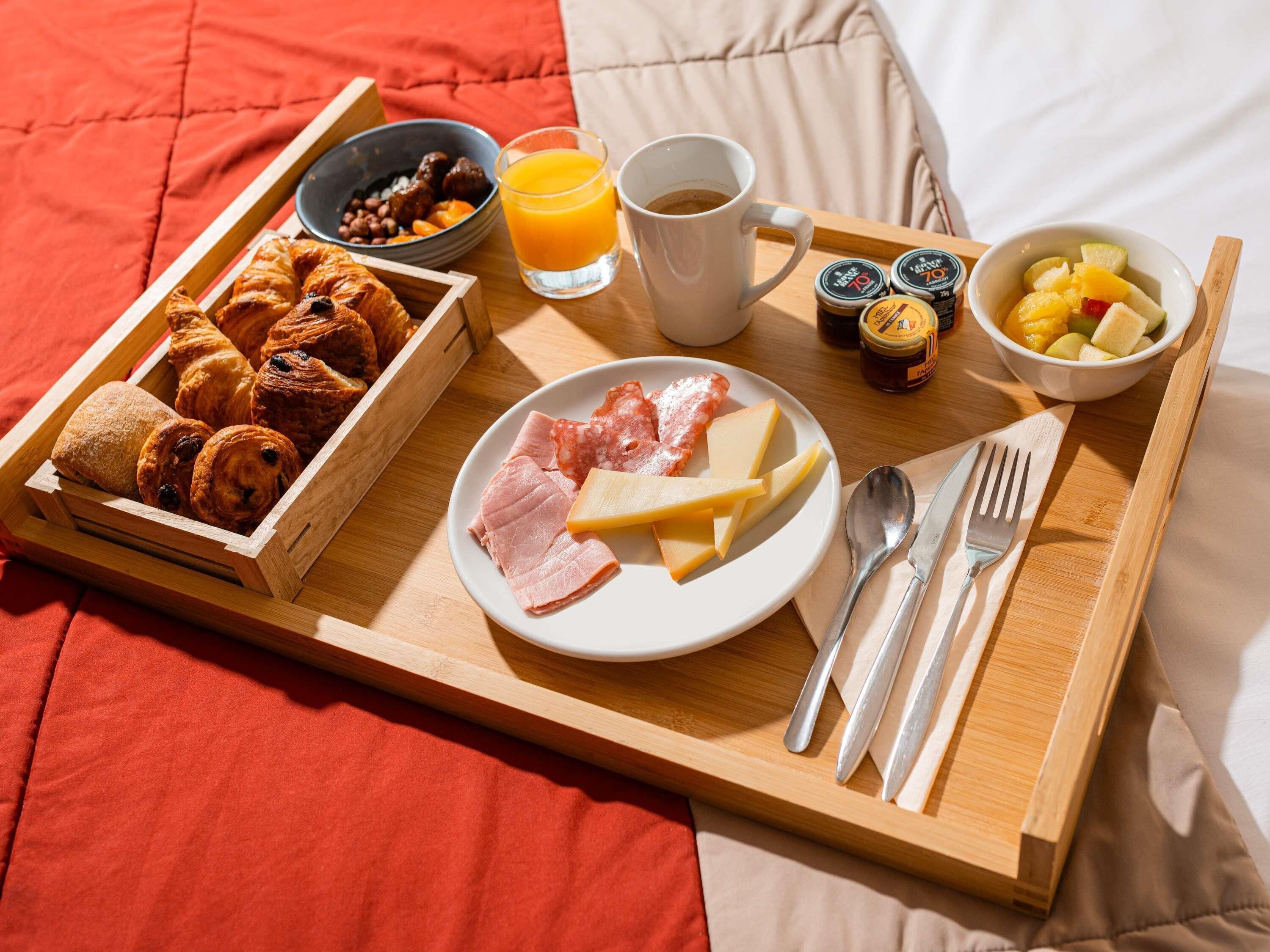 A breakfast tray with croissants, cheese, ham, and fruit on a bed.