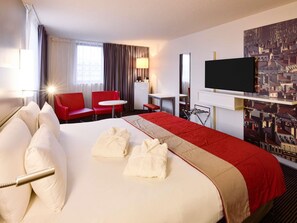A hotel room with a large bed, red chairs, a desk, a TV, and a cityscape painting. - Mercure Lyon Centre Saxe Lafayette (Lyon)