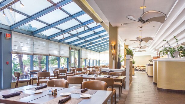 A spacious indoor dining area with tables and chairs, large windows, and ceiling fans. - Hilton Melbourne, FL (Melbourne)