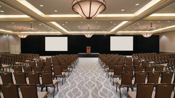 A conference room with rows of chairs, a stage with a podium, and two large screens.