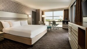 A hotel room with a large bed, a desk, a chair, a TV, and a window with curtains. - Hilton Melbourne, FL (Melbourne)