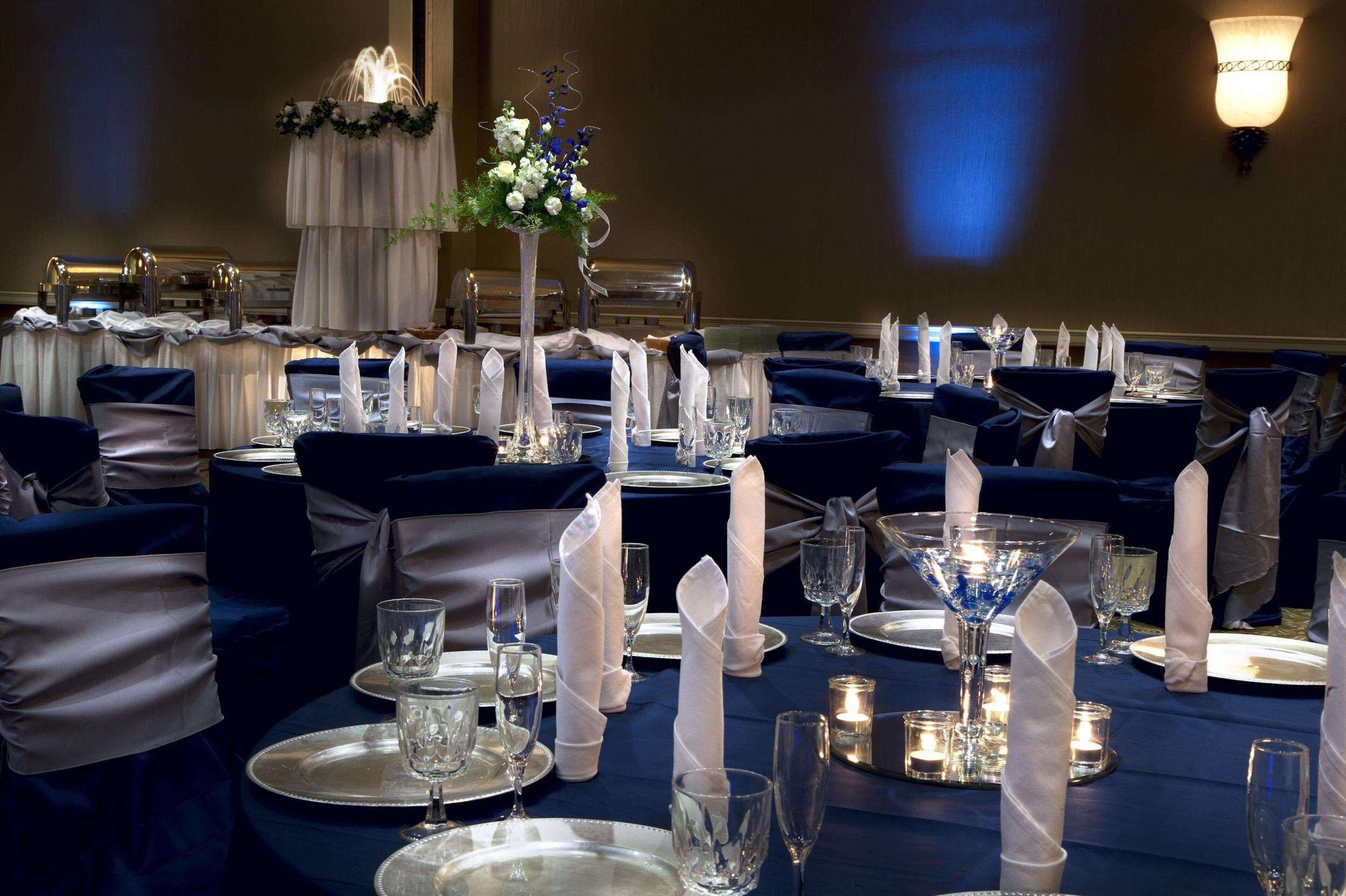 Un salón de banquetes con mesas redondas dispuestas para un evento formal, con servilletas blancas, cristalería de cristal y centros de mesa florales.