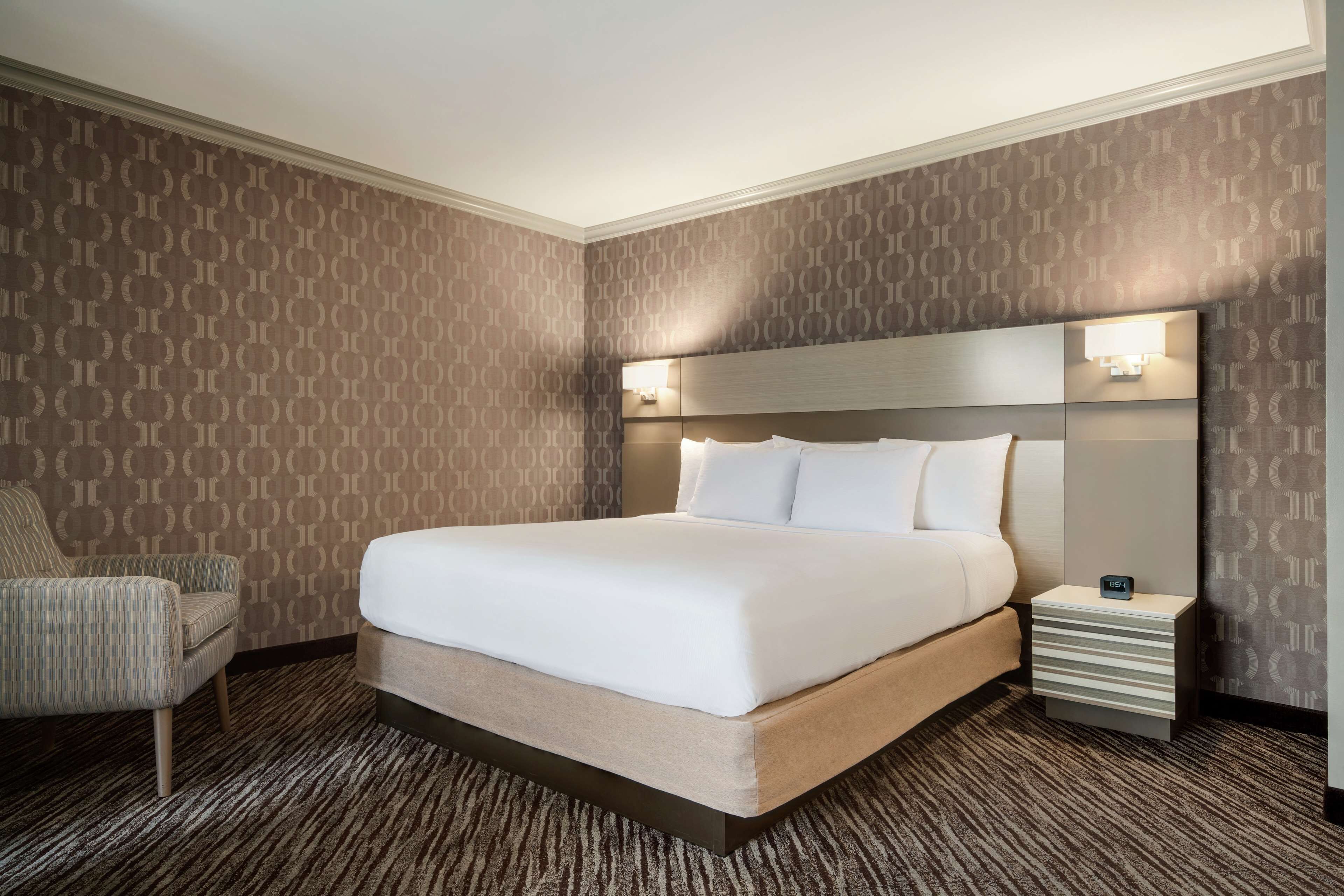 Una habitación de hotel con una cama grande, una mesita de noche, una silla y papel tapiz estampado.