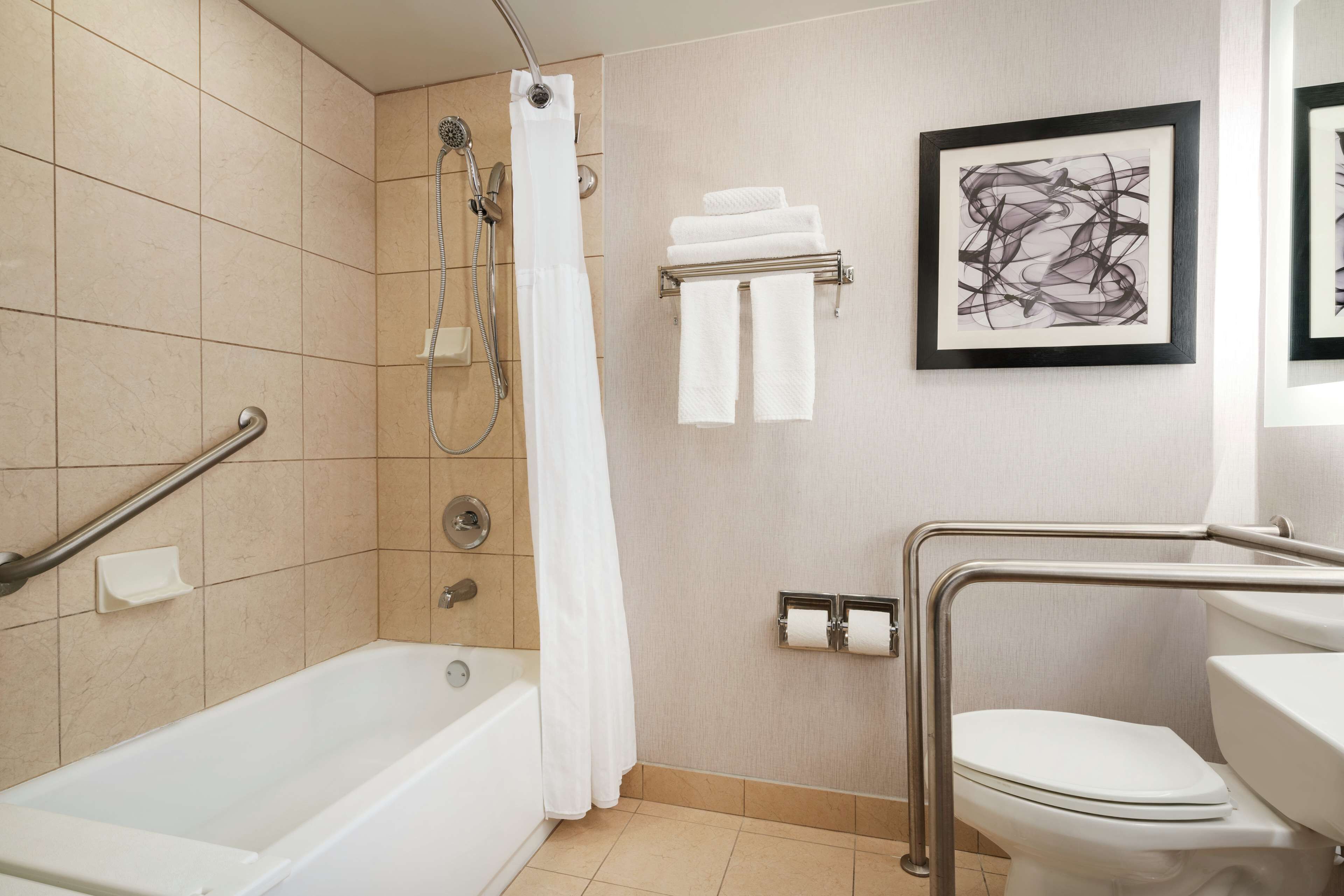 Un baño moderno con bañera, ducha, inodoro y barras de apoyo.