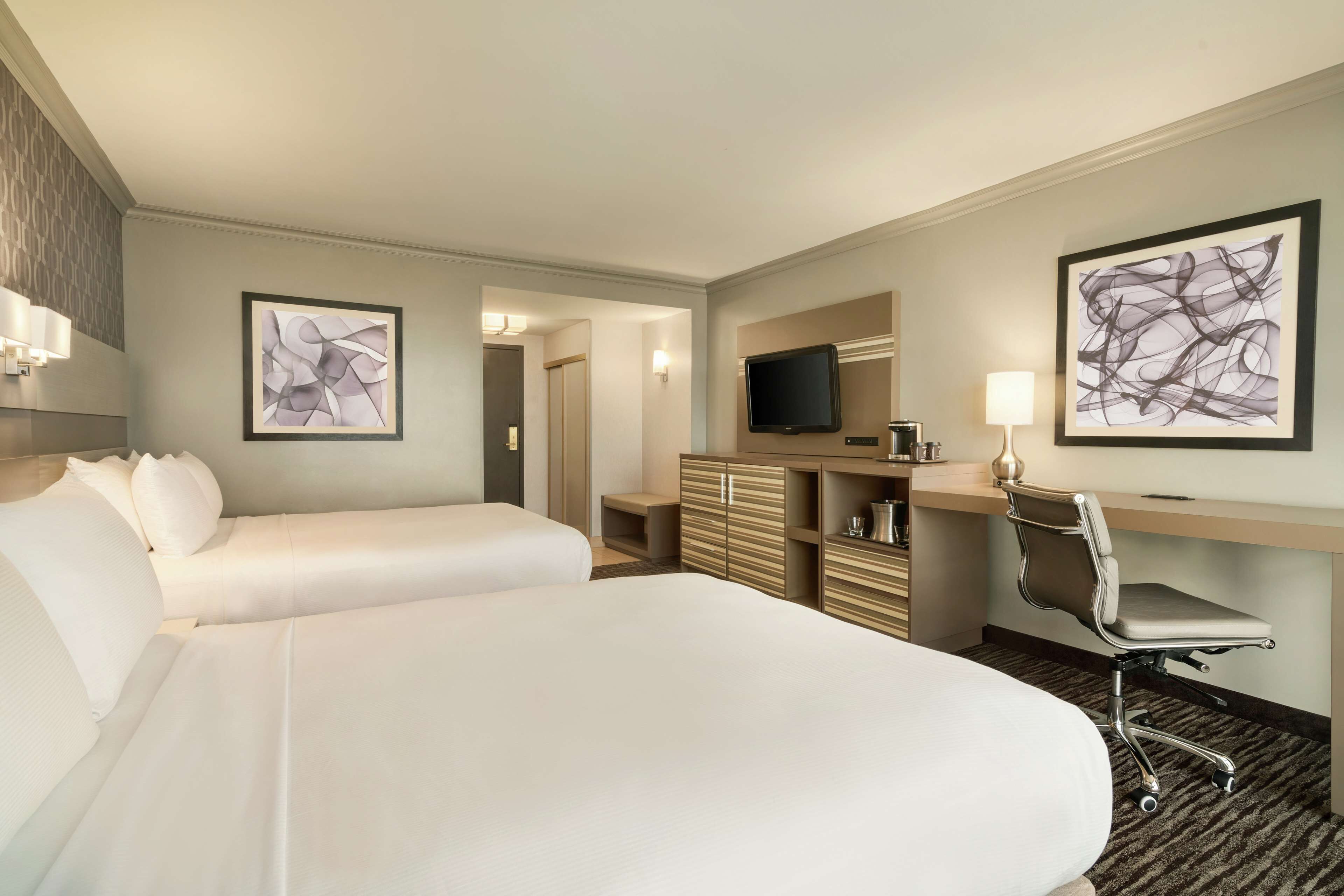 Ein Hotelzimmer mit zwei Betten, einem Schreibtisch mit Stuhl, einem Fernseher und Bildern an den Wänden.