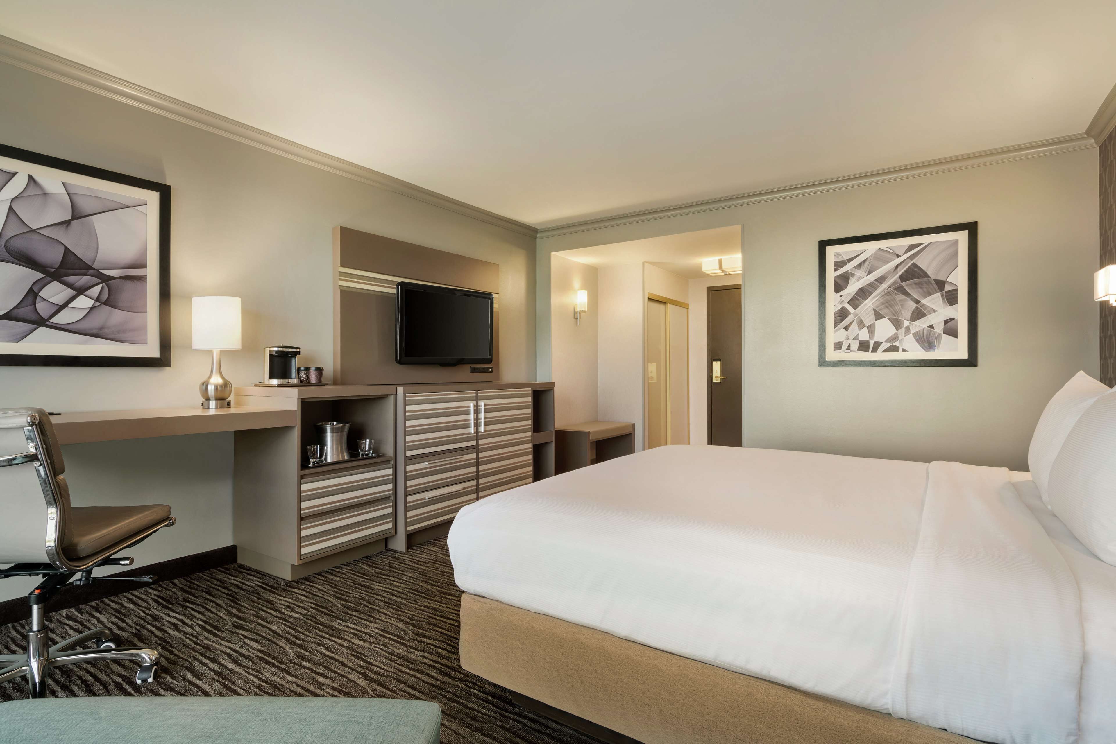 Une chambre d’hôtel avec un grand lit, un bureau avec une chaise, une télévision et un minibar.