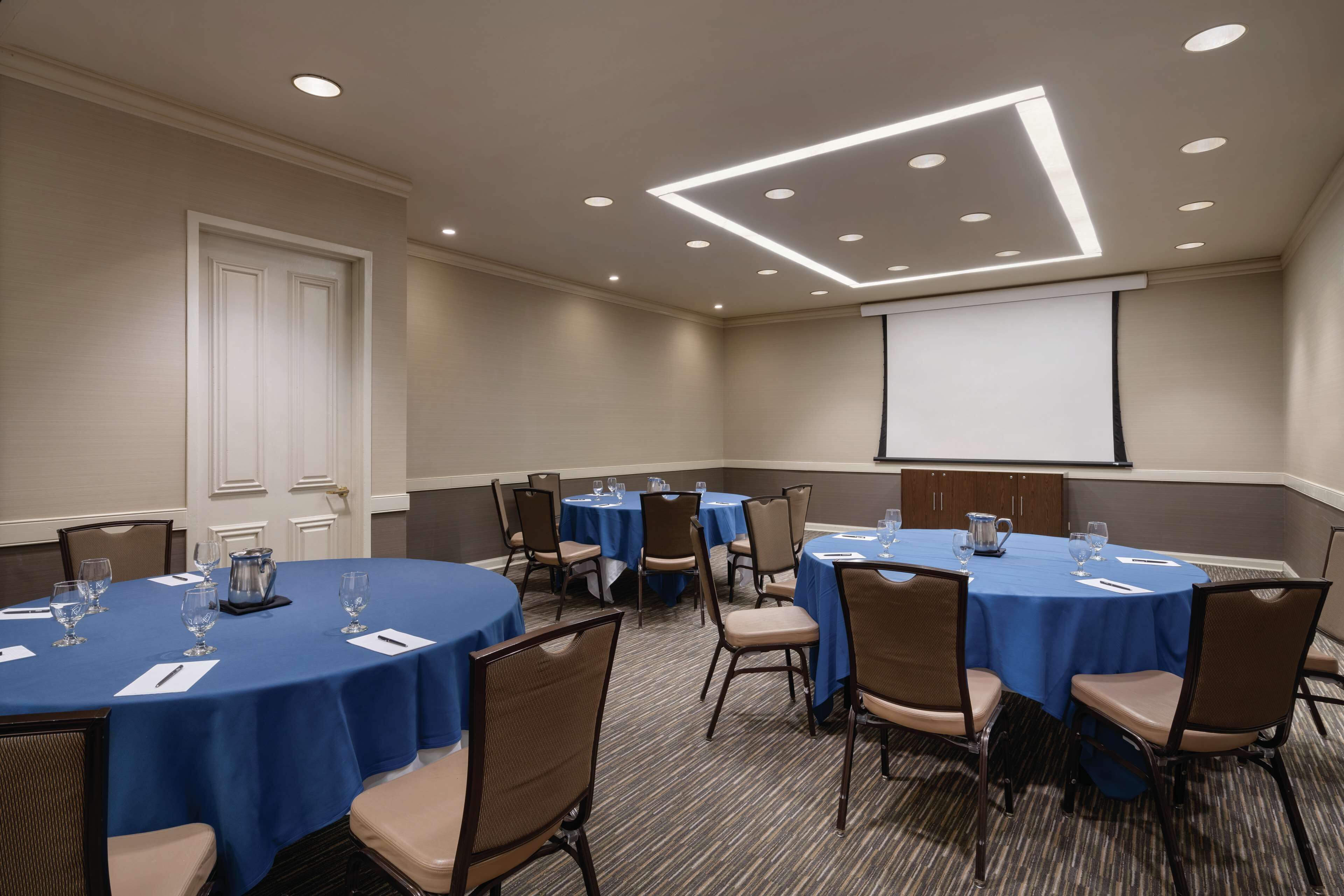 Un salón de conferencias con mesas redondas, sillas y una pantalla para proyector.