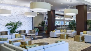 A modern lobby with white sofas, gold accents, and large pendant lights. - Hilton Melbourne, FL (Melbourne)