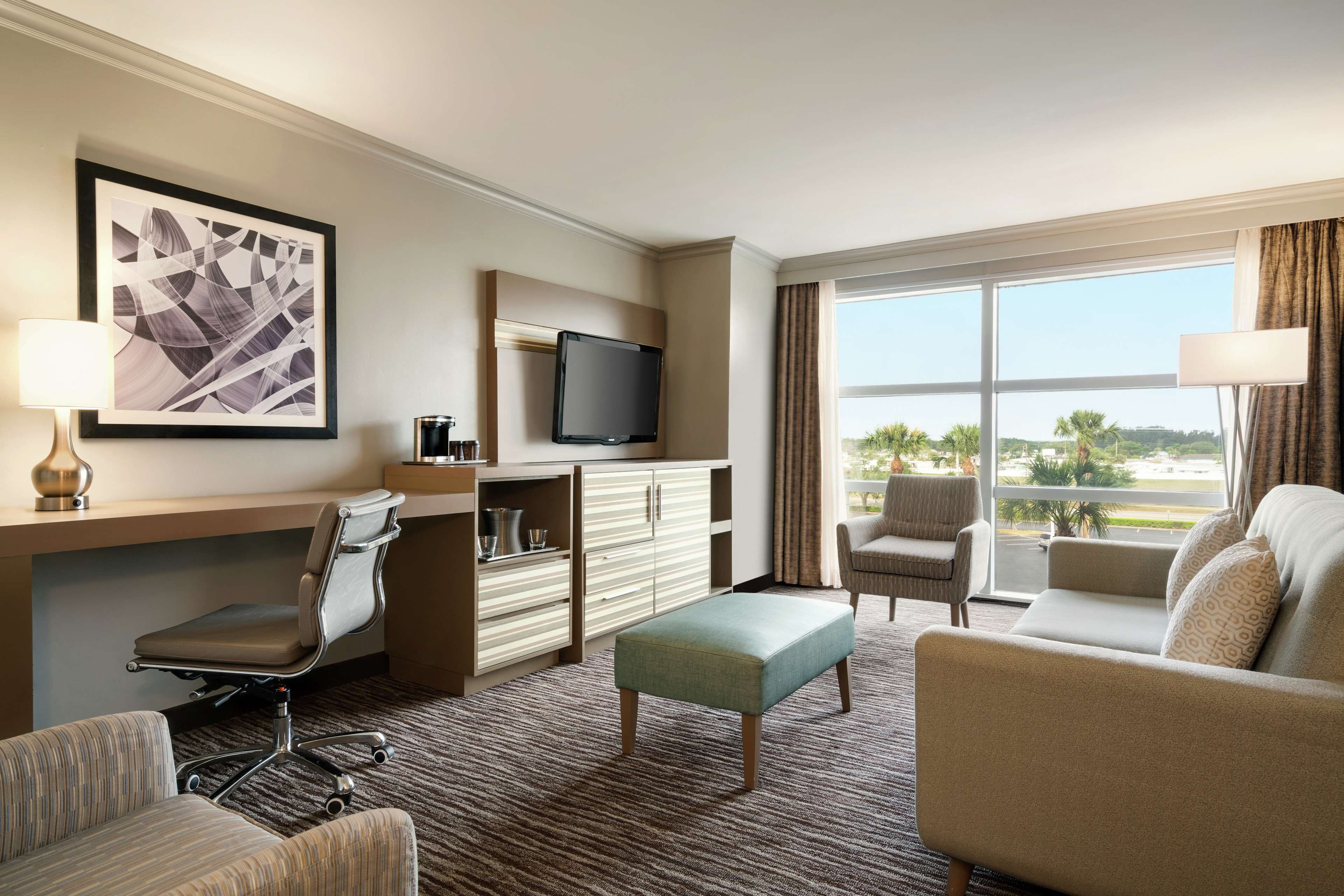 A hotel room with a desk, a television, a sofa, and a view of the outdoors.