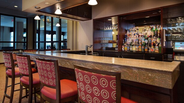 Eine Bar mit einer langen Theke, mehreren Barhocker und einer gut sortierten Bar mit verschiedenen Flaschen und Gläsern.