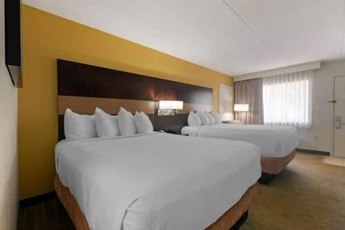 A hotel room with two beds, a wooden headboard, a window with curtains, and a door.