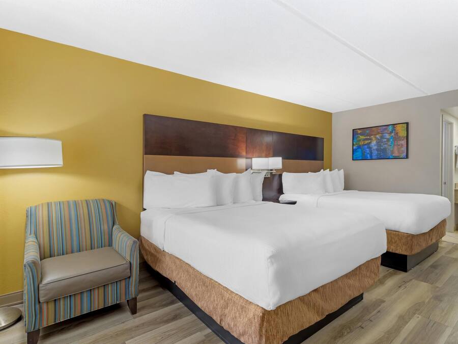 A hotel room with a large bed, a chair, a floor lamp, and a painting on the wall.