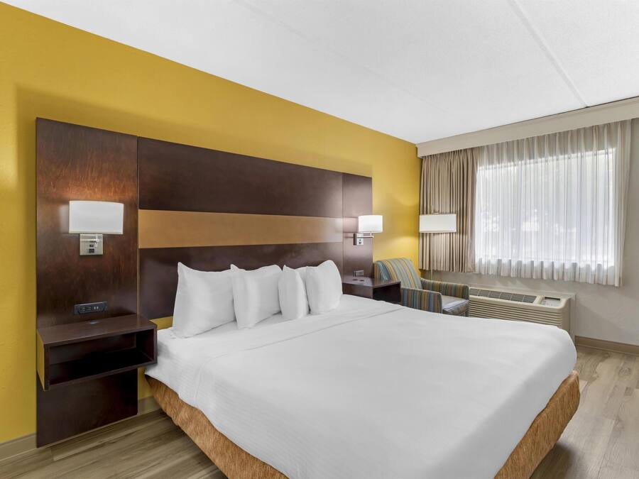 Quarto de hotel com uma cama grande, mesas de cabeceira, uma escrivaninha e uma janela com cortinas.