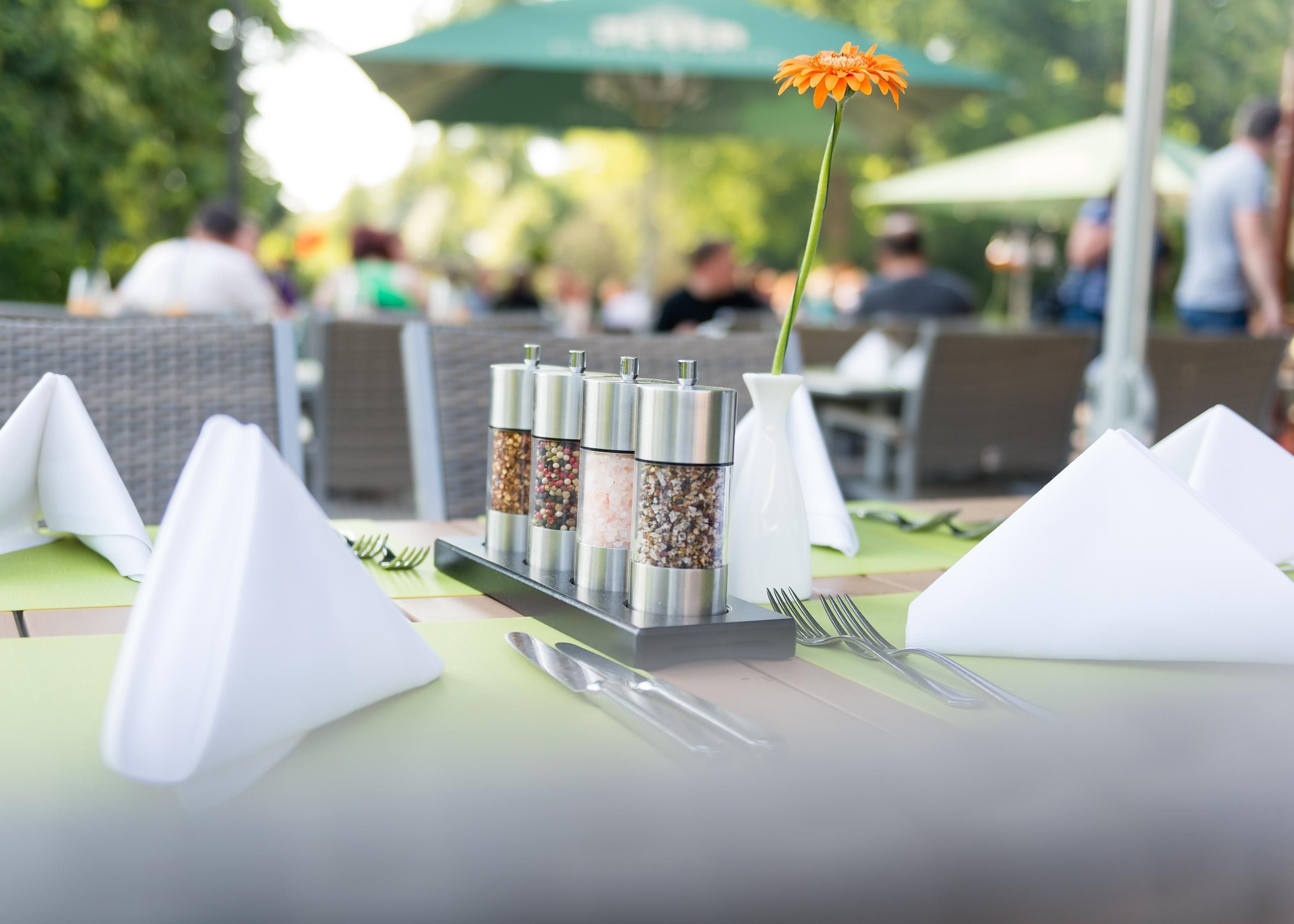 Une table dressée avec des condiments, une fleur et des couverts.