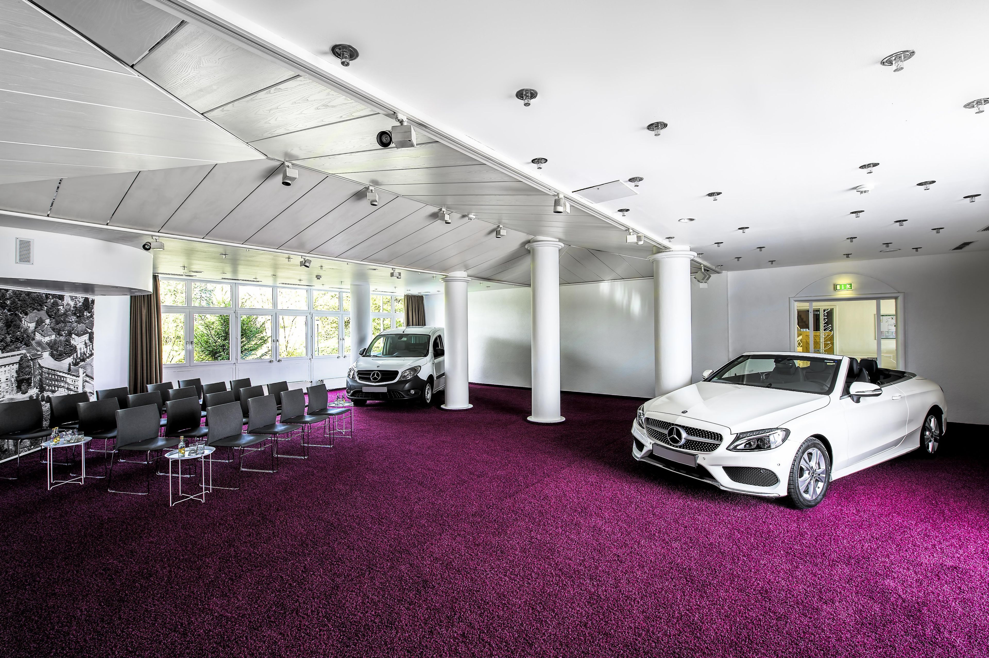 A conference room with a white convertible parked inside, large windows, and a purple carpet.