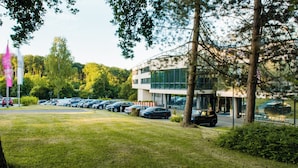 A parking lot with several cars, a modern building with large windows, and trees in the background.