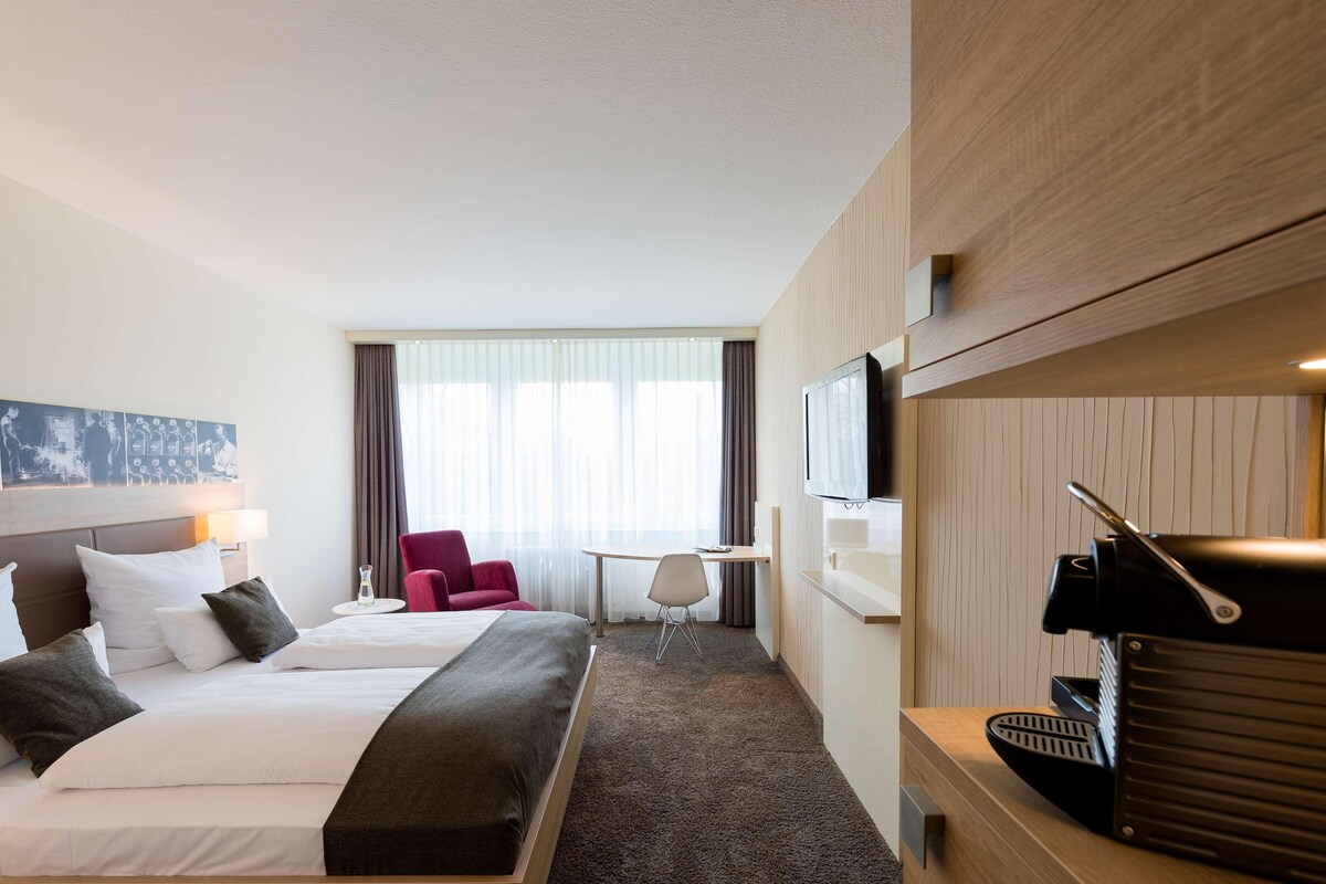 A hotel room with a bed, a desk, a chair, a television, and a window with curtains.