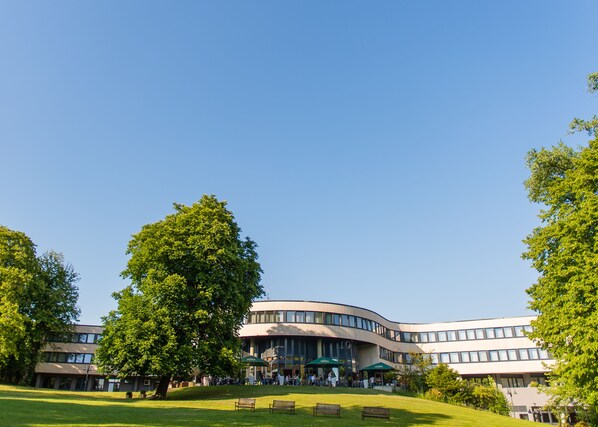 A modern building with a curved facade, surrounded by a grassy area with benches and trees. - Best Western Plus Parkhotel Velbert (Velbert)